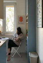 Beżowe składane krzesło z czarnymi nogami i podłokietnikami, z amortyzowanym siedziskiem i oparciem.